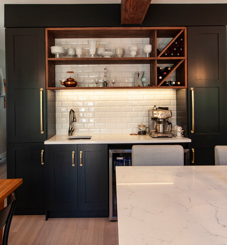 This is an example of a medium sized classic l-shaped kitchen/diner in Other with a submerged sink, shaker cabinets, black cabinets, engineered stone countertops, white splashback, ceramic splashback, stainless steel appliances, light hardwood flooring, an island, white floors and white worktops.