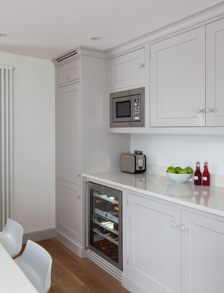 Zweizeilige, Mittelgroße Moderne Wohnküche mit Schrankfronten mit vertiefter Füllung, grauen Schränken, Quarzit-Arbeitsplatte, Küchenrückwand in Weiß, Glasrückwand, Küchengeräten aus Edelstahl, hellem Holzboden und Kücheninsel in London