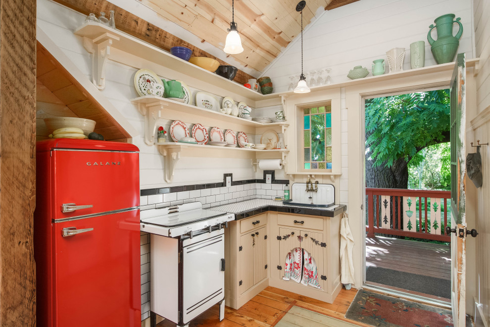 Small farmhouse l-shaped kitchen in Portland with a built-in sink, flat-panel cabinets, beige cabinets, tile countertops, white splashback, metro tiled splashback, coloured appliances, medium hardwood flooring, no island, brown floors, white worktops, a vaulted ceiling and a wood ceiling.
