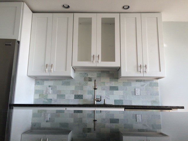 This is an example of a small contemporary galley kitchen/diner in New York with a submerged sink, shaker cabinets, white cabinets, granite worktops, blue splashback, stone tiled splashback, stainless steel appliances, porcelain flooring and no island.