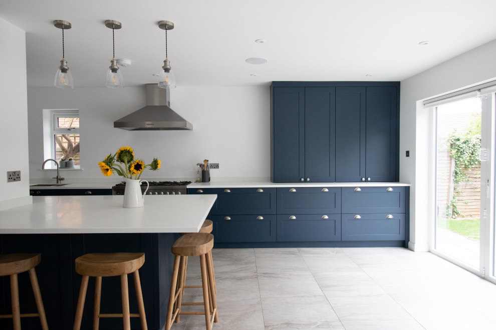 Immagine di una cucina chic con lavello da incasso, ante in stile shaker, ante blu, top in superficie solida, elettrodomestici in acciaio inossidabile, pavimento con piastrelle in ceramica, pavimento grigio e top bianco