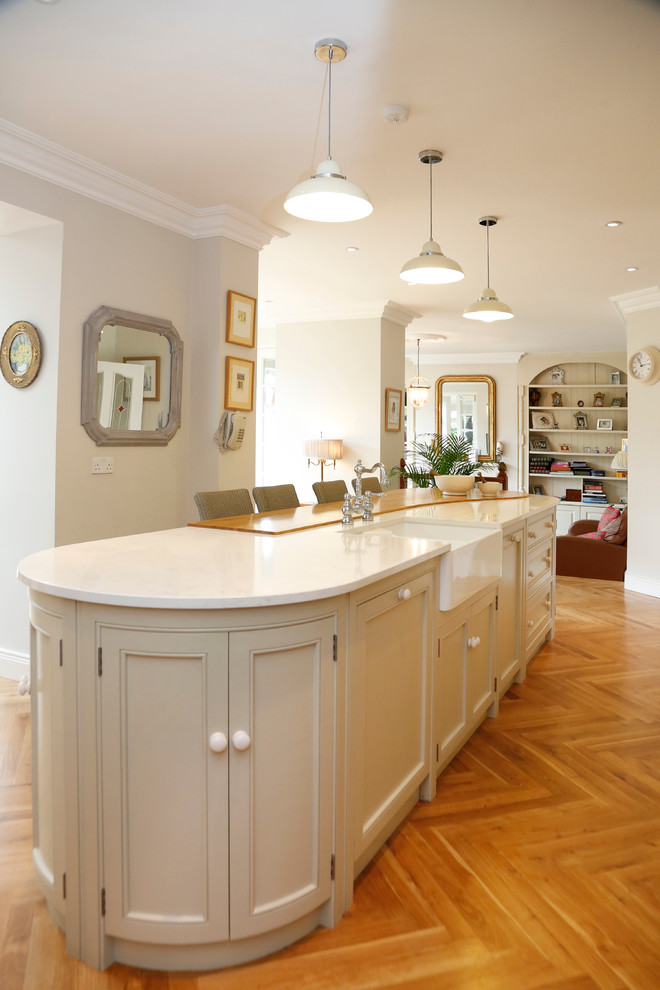 Example of a large classic l-shaped medium tone wood floor kitchen design in Cork with a farmhouse sink, recessed-panel cabinets, white cabinets, quartz countertops, stainless steel appliances and an island