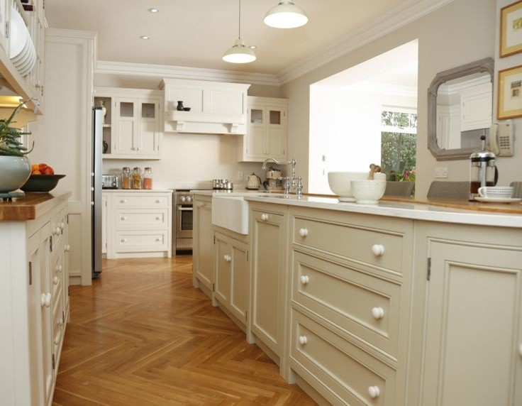Large elegant l-shaped medium tone wood floor kitchen photo in Cork with a farmhouse sink, recessed-panel cabinets, white cabinets, quartz countertops, stainless steel appliances and an island