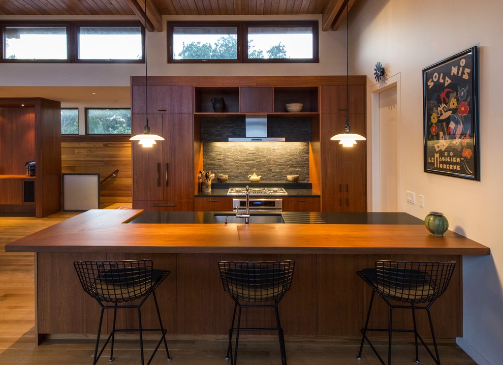 Open concept kitchen - mid-sized 1960s galley medium tone wood floor and brown floor open concept kitchen idea in Boston with a single-bowl sink, flat-panel cabinets, medium tone wood cabinets, wood countertops, black backsplash, stone tile backsplash, paneled appliances, an island and black countertops