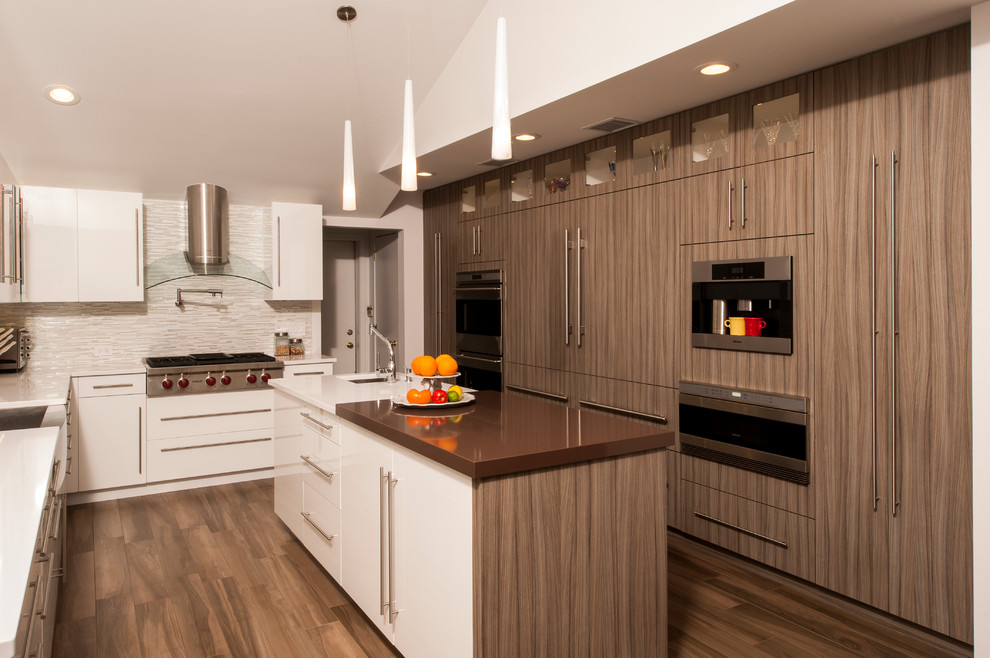 Bild på ett funkis u-kök, med en enkel diskho, släta luckor, vita skåp, flerfärgad stänkskydd och rostfria vitvaror
