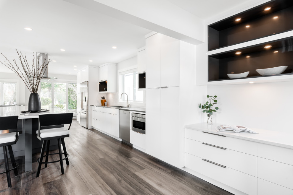 Idéer för att renovera ett stort funkis grå linjärt grått kök med öppen planlösning, med en undermonterad diskho, släta luckor, vita skåp, bänkskiva i kvarts, vitt stänkskydd, stänkskydd i sten, rostfria vitvaror, vinylgolv, en köksö och brunt golv