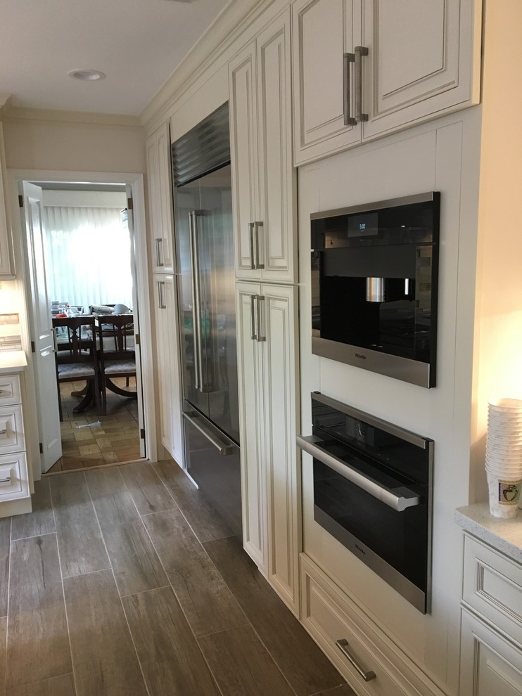Kitchen pantry - huge traditional single-wall porcelain tile and brown floor kitchen pantry idea in New York with a farmhouse sink, raised-panel cabinets, beige cabinets, quartzite countertops, multicolored backsplash, glass tile backsplash, stainless steel appliances and an island