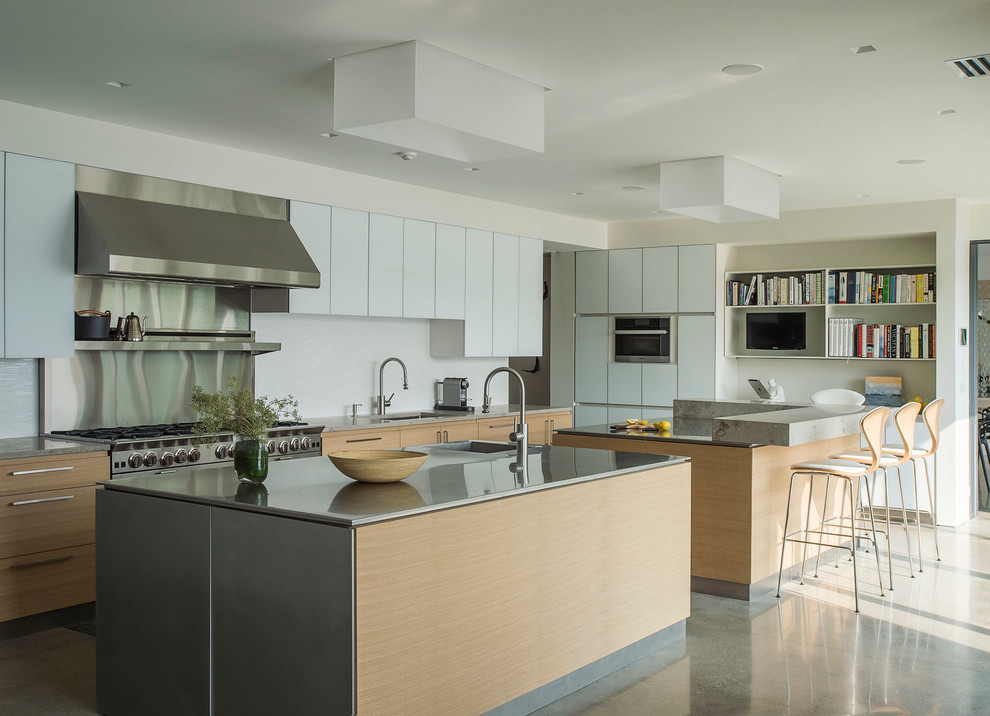 Modern l-shaped kitchen/diner in New York with a submerged sink, flat-panel cabinets, white cabinets, stainless steel worktops, white splashback, stone slab splashback, stainless steel appliances, concrete flooring and multiple islands.