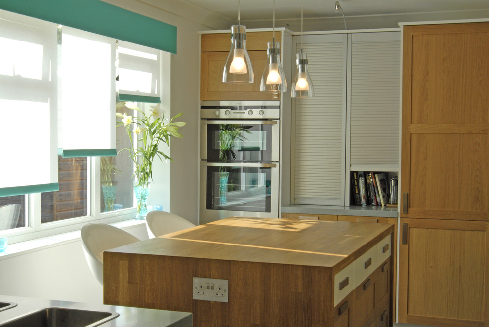 Contemporary kitchen in London with stainless steel appliances, medium wood cabinets and wood worktops.