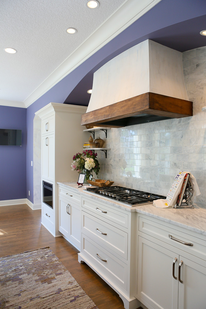 Photo of a large classic single-wall open plan kitchen in Minneapolis with a submerged sink, recessed-panel cabinets, white cabinets, marble worktops, grey splashback, stainless steel appliances, medium hardwood flooring and an island.