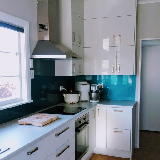 Bild på ett mellanstort funkis kök, med en enkel diskho, släta luckor, vita skåp, laminatbänkskiva, blått stänkskydd, glaspanel som stänkskydd, svarta vitvaror, vinylgolv och brunt golv