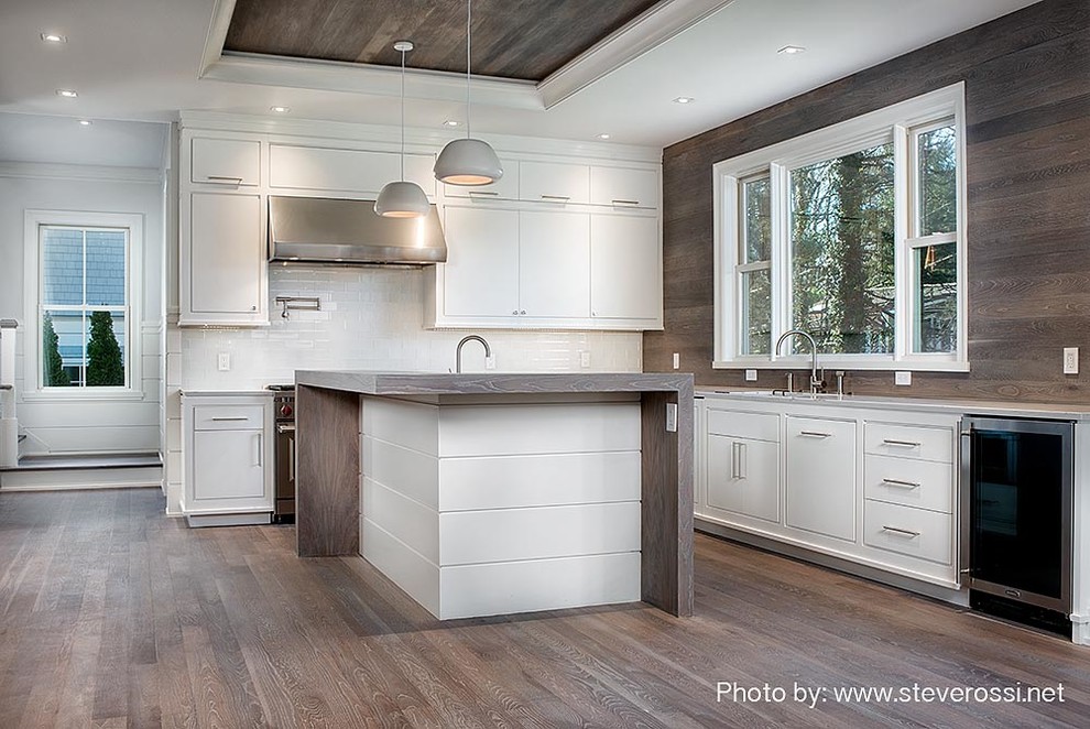 This is an example of a large classic u-shaped open plan kitchen in New York with a submerged sink, flat-panel cabinets, white cabinets, quartz worktops, white splashback, glass tiled splashback, stainless steel appliances, light hardwood flooring, an island and brown floors.