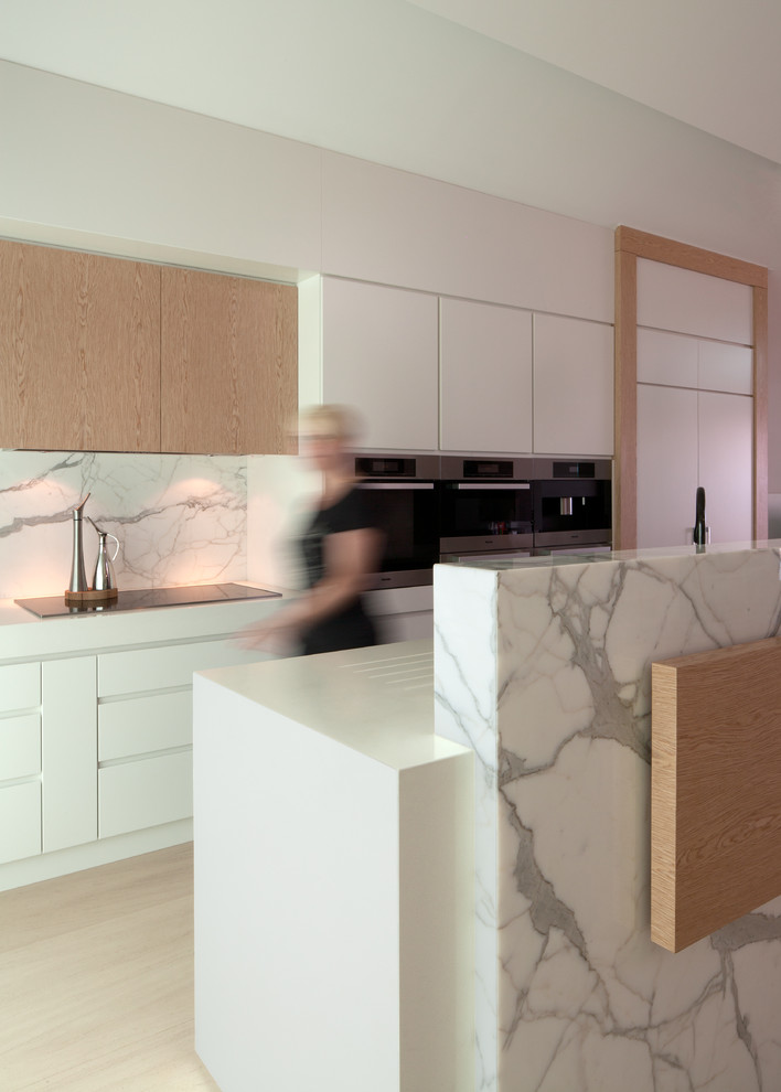 Réalisation d'une cuisine minimaliste avec un placard à porte plane, des portes de placard blanches, un électroménager en acier inoxydable et une crédence en marbre.