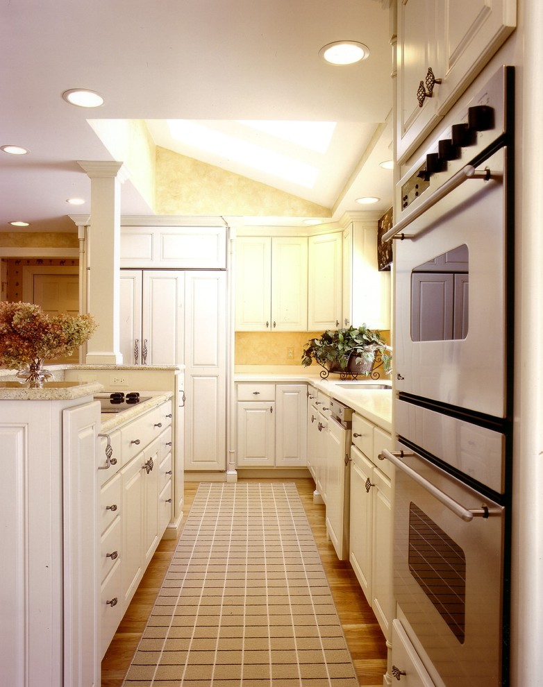 Example of a mid-sized transitional l-shaped medium tone wood floor kitchen design in Boston with an undermount sink, raised-panel cabinets, white cabinets, granite countertops, stainless steel appliances and an island