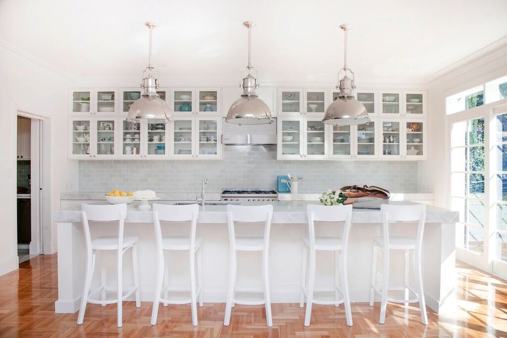 Klassisk inredning av ett mellanstort kök, med en undermonterad diskho, luckor med glaspanel, vita skåp, marmorbänkskiva, grått stänkskydd, stänkskydd i glaskakel, rostfria vitvaror, mellanmörkt trägolv och en köksö