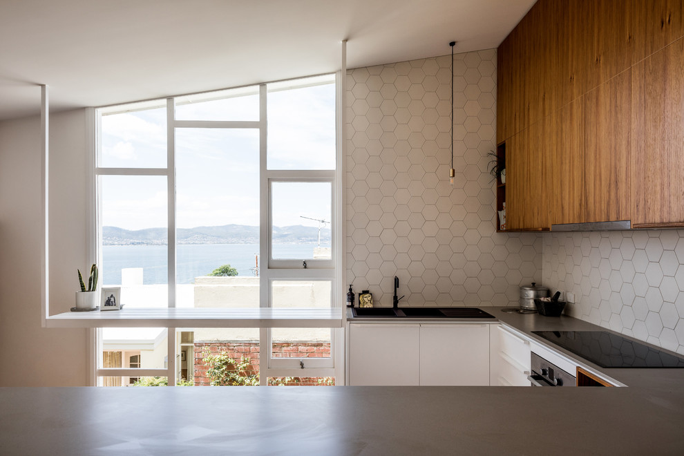 Moderne Küche in U-Form mit Einbauwaschbecken, flächenbündigen Schrankfronten, hellbraunen Holzschränken, Küchenrückwand in Weiß und grauer Arbeitsplatte in Hobart