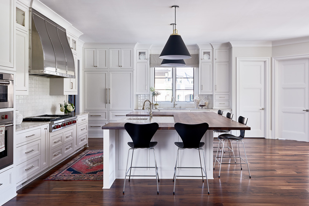 Bild på ett stort vintage kök, med vita skåp, vitt stänkskydd, rostfria vitvaror, en köksö, brunt golv, mellanmörkt trägolv, luckor med infälld panel och träbänkskiva