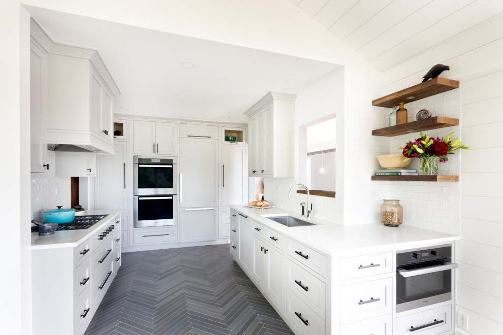 Photo of a beach style u-shaped kitchen in Vancouver with a submerged sink, shaker cabinets, white cabinets, white splashback, metro tiled splashback, integrated appliances, no island, grey floors and white worktops.