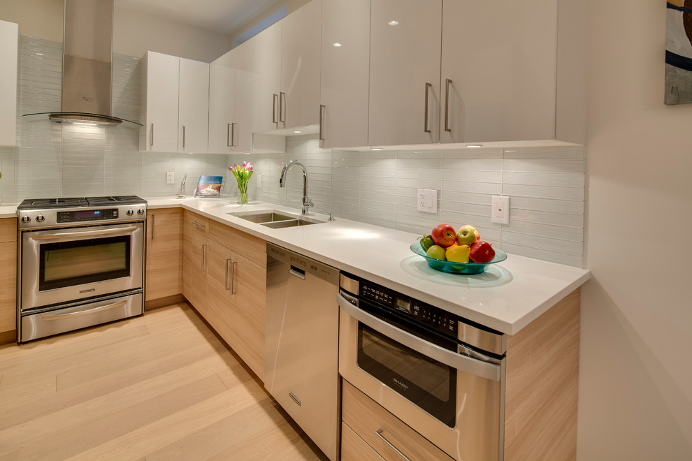Inspiration for a small contemporary l-shaped light wood floor kitchen remodel in Vancouver with a double-bowl sink, flat-panel cabinets, light wood cabinets, white backsplash, glass tile backsplash and stainless steel appliances