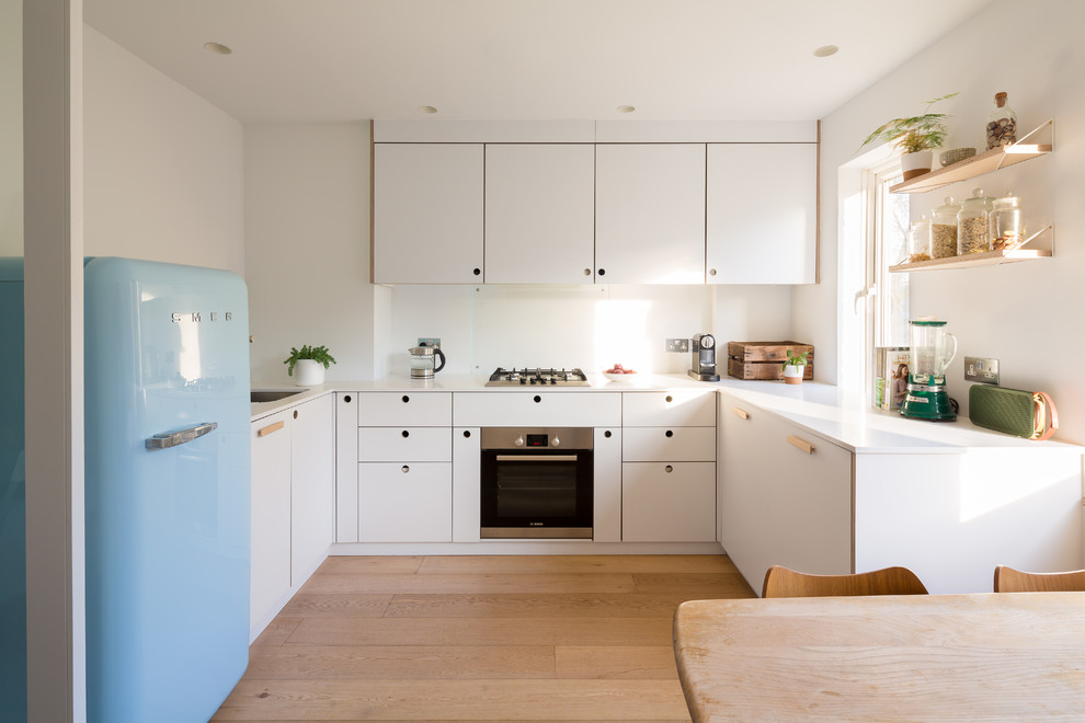 Inredning av ett skandinaviskt litet vit vitt kök, med en undermonterad diskho, släta luckor, vita skåp, ljust trägolv, beiget golv, vitt stänkskydd, glaspanel som stänkskydd och färgglada vitvaror