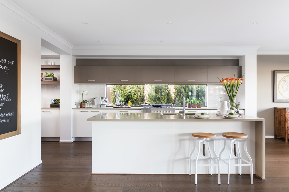 Modern inredning av ett l-kök, med en undermonterad diskho, släta luckor, vita skåp, vitt stänkskydd, mörkt trägolv och en köksö
