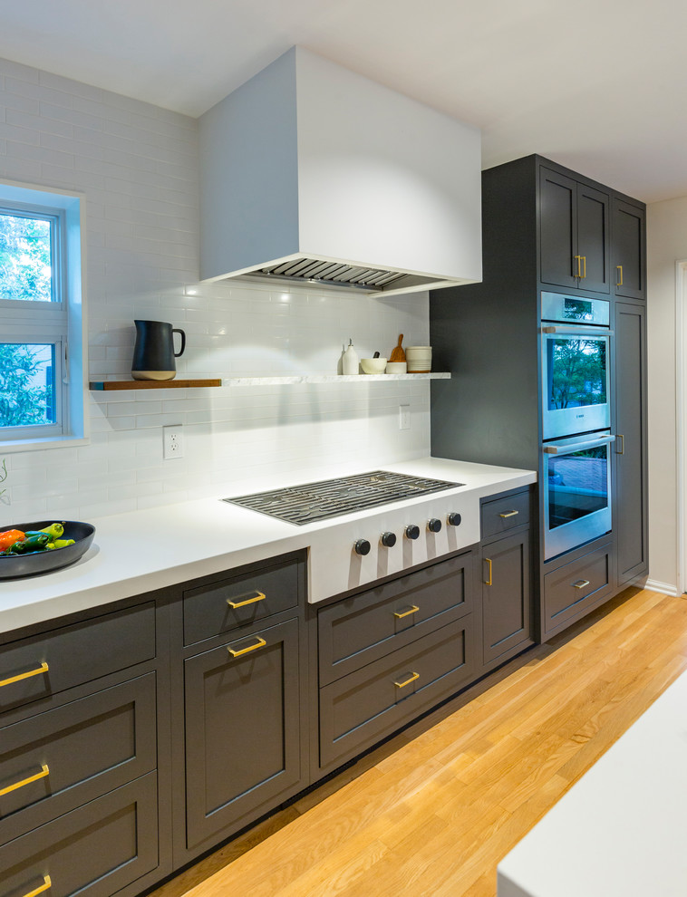 Minimalist l-shaped medium tone wood floor and brown floor open concept kitchen photo in Cincinnati with an undermount sink, recessed-panel cabinets, blue cabinets, quartz countertops, white backsplash, ceramic backsplash, stainless steel appliances, an island and white countertops