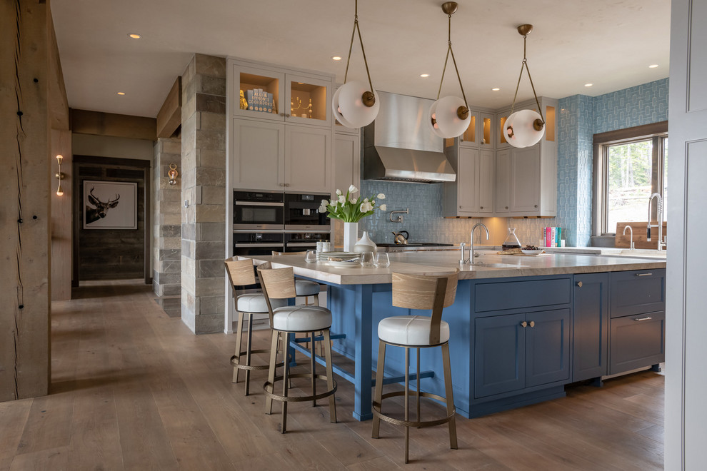 Diseño de cocina rústica con armarios estilo shaker, puertas de armario grises, salpicadero azul, una isla, encimeras grises y suelo de madera clara