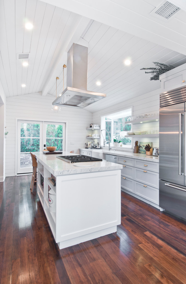 Photo of a medium sized farmhouse galley kitchen/diner in Los Angeles with a belfast sink, shaker cabinets, white cabinets, marble worktops, white splashback, wood splashback, stainless steel appliances, painted wood flooring and an island.