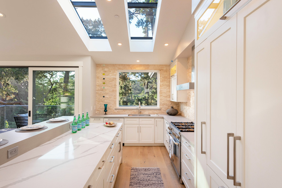 Foto på ett mellanstort funkis grå kök och matrum, med en undermonterad diskho, skåp i shakerstil, vita skåp, beige stänkskydd, rostfria vitvaror, mellanmörkt trägolv och en köksö