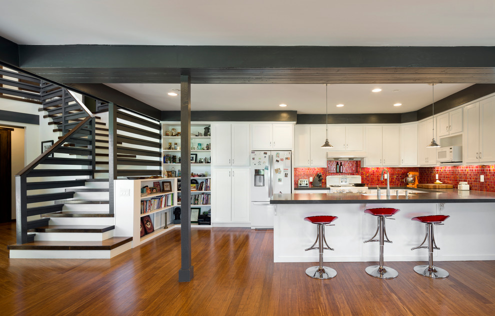 This is an example of a contemporary u-shaped kitchen in Los Angeles with shaker cabinets, white cabinets, red splashback, white appliances, dark hardwood flooring and a breakfast bar.