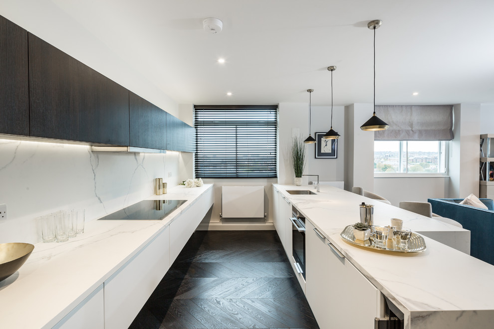 Inspiration for a contemporary galley kitchen in London with a submerged sink, flat-panel cabinets, white cabinets, white splashback, black appliances, dark hardwood flooring and an island.