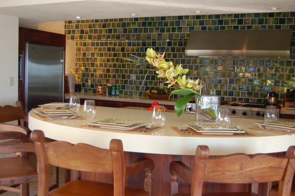Esempio di una cucina tropicale con lavello sottopiano, ante a persiana, ante in legno scuro, top in superficie solida, paraspruzzi verde, paraspruzzi con piastrelle in ceramica e elettrodomestici in acciaio inossidabile
