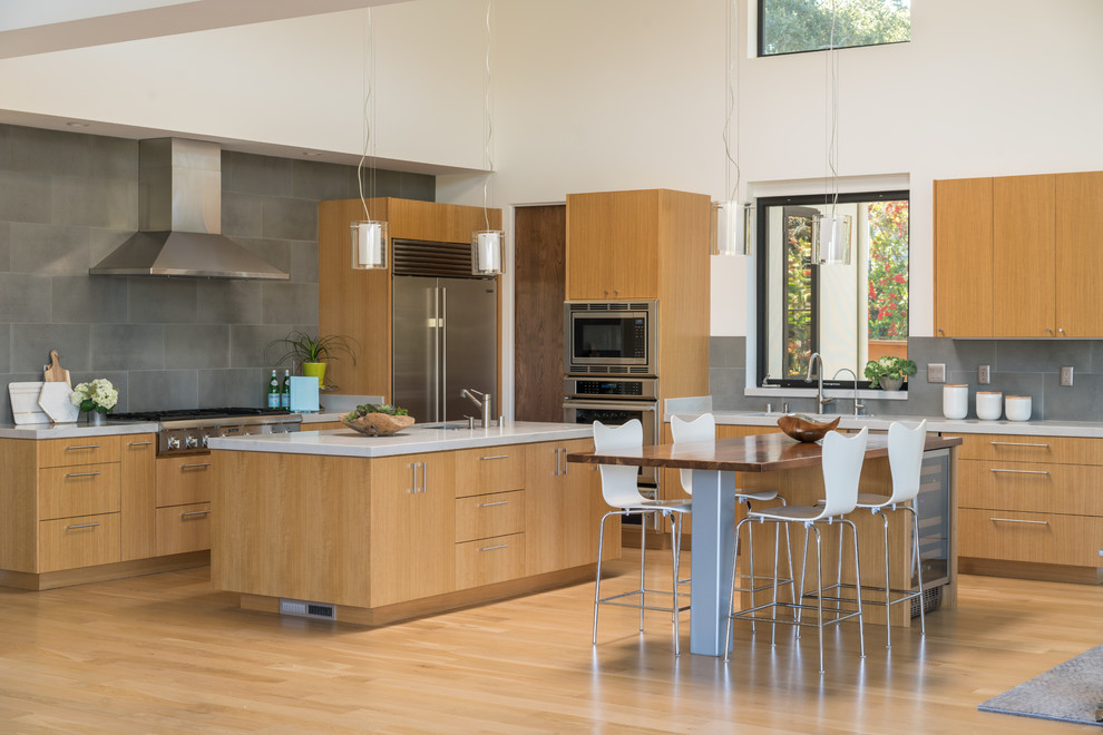 Example of a trendy l-shaped light wood floor and brown floor eat-in kitchen design in San Francisco with an undermount sink, flat-panel cabinets, medium tone wood cabinets, gray backsplash, stainless steel appliances and two islands