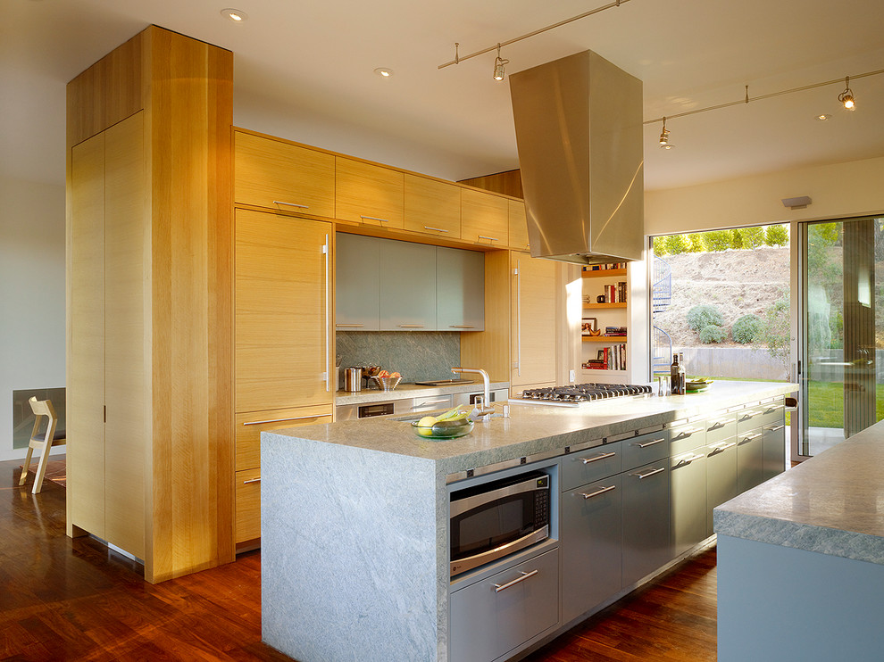 Diseño de cocina moderna de tamaño medio con armarios con paneles lisos, puertas de armario de madera clara, salpicadero verde, suelo de madera oscura, una isla y electrodomésticos de acero inoxidable