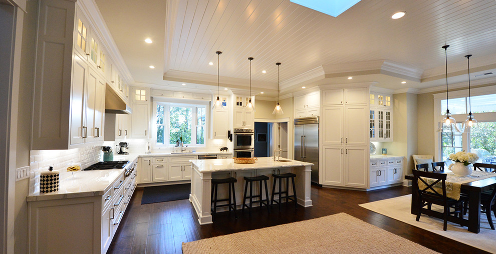 Large classic l-shaped kitchen/diner in San Francisco with a submerged sink, shaker cabinets, white cabinets, composite countertops, white splashback, metro tiled splashback, stainless steel appliances, vinyl flooring and an island.