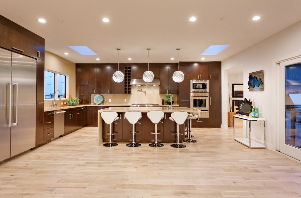 This is an example of a large contemporary l-shaped kitchen in San Francisco with a submerged sink, flat-panel cabinets, brown cabinets, beige splashback, stainless steel appliances, light hardwood flooring, an island, beige floors and beige worktops.