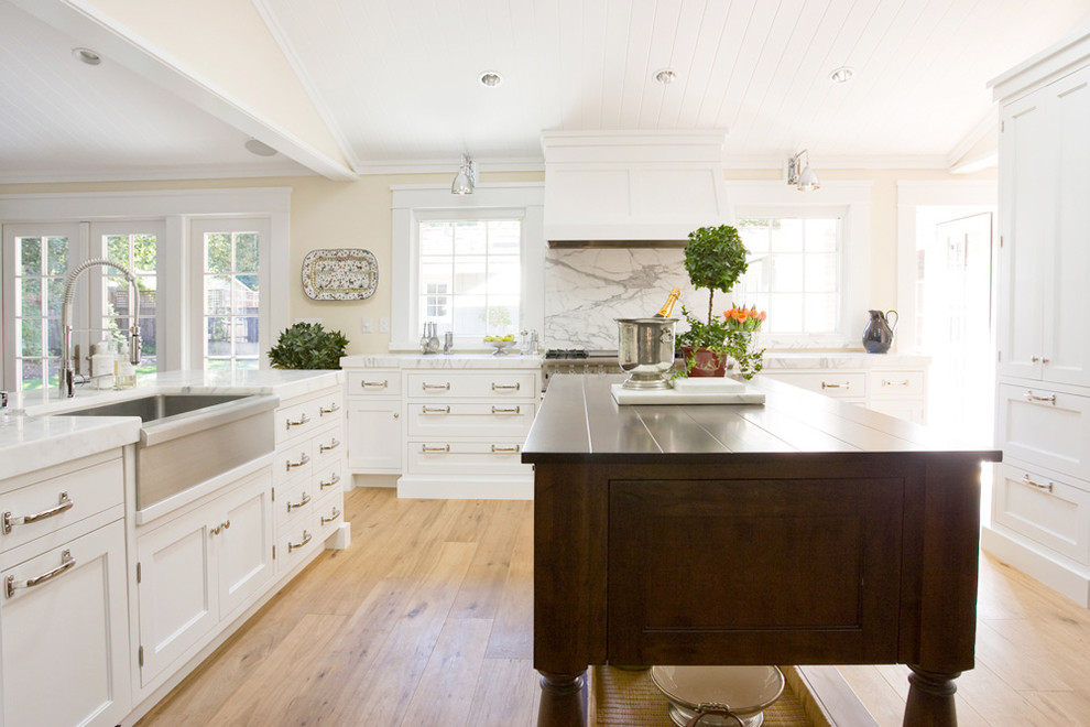 Example of a mid-sized transitional u-shaped light wood floor and brown floor eat-in kitchen design in San Francisco with a farmhouse sink, recessed-panel cabinets, white cabinets, marble countertops, multicolored backsplash, stone slab backsplash, stainless steel appliances and an island