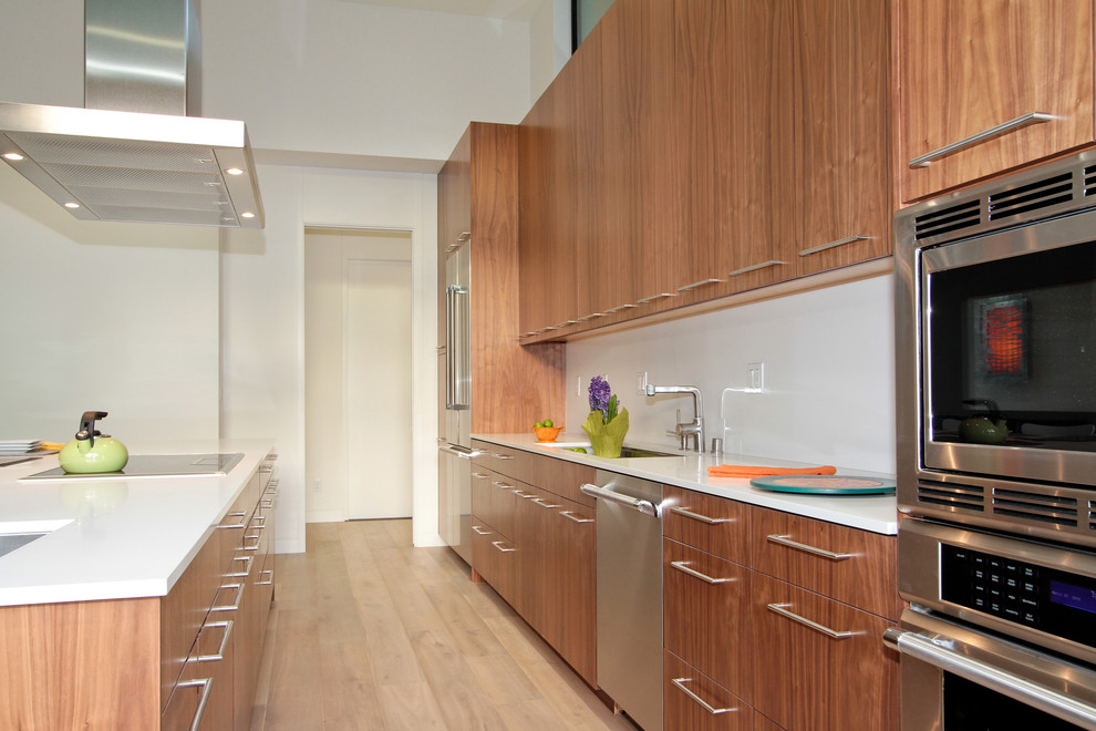 Foto de cocina minimalista con armarios con paneles lisos, puertas de armario de madera oscura, salpicadero blanco y electrodomésticos de acero inoxidable