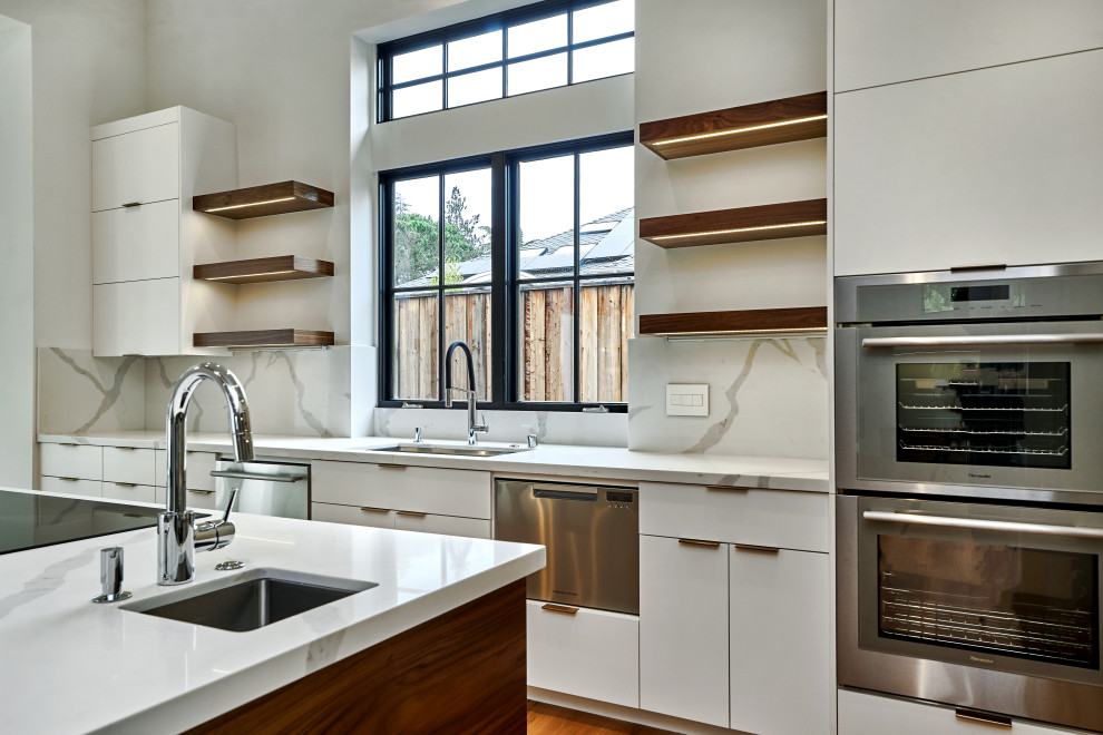 Mid-sized minimalist single-wall light wood floor and brown floor enclosed kitchen photo in San Francisco with an undermount sink, flat-panel cabinets, white cabinets, quartz countertops, white backsplash, stone slab backsplash, stainless steel appliances, an island and white countertops