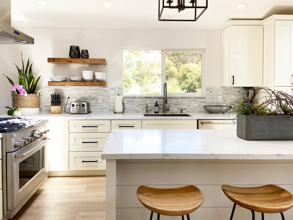 Klassisk inredning av ett mellanstort vit vitt l-kök, med en undermonterad diskho, skåp i shakerstil, vita skåp, bänkskiva i kvarts, flerfärgad stänkskydd, stänkskydd i mosaik, rostfria vitvaror, vinylgolv, en köksö och brunt golv