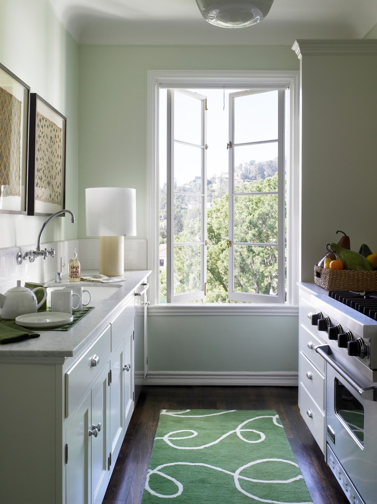 Cette image montre une petite cuisine parallèle traditionnelle fermée avec un évier encastré, une crédence blanche, un électroménager en acier inoxydable, parquet foncé, un placard à porte shaker, des portes de placard blanches, aucun îlot et un plan de travail en quartz modifié.