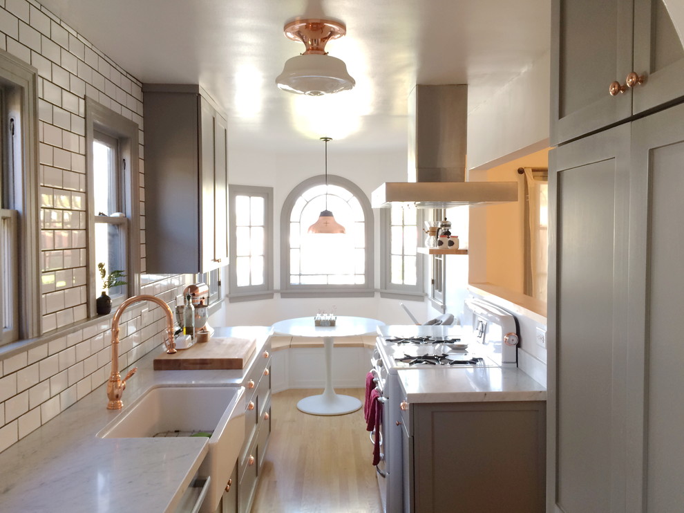 Small farmhouse u-shaped kitchen/diner in Los Angeles with a belfast sink, shaker cabinets, grey cabinets, marble worktops, white splashback, metro tiled splashback, stainless steel appliances, light hardwood flooring, no island and beige floors.