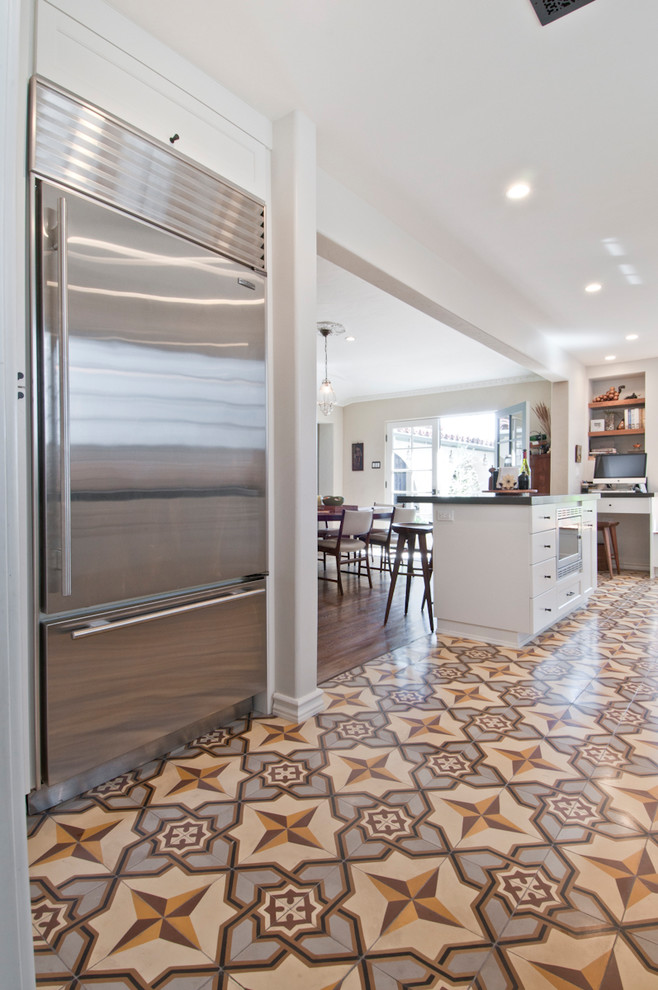This is an example of a medium sized traditional galley kitchen/diner in Los Angeles with a submerged sink, shaker cabinets, white cabinets, quartz worktops, white splashback, ceramic splashback, stainless steel appliances, cement flooring, an island and yellow floors.