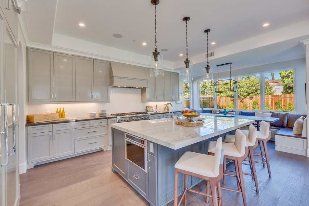 Classic l-shaped kitchen/diner in Los Angeles with a belfast sink, recessed-panel cabinets, beige cabinets, white splashback, integrated appliances, light hardwood flooring, an island and beige floors.