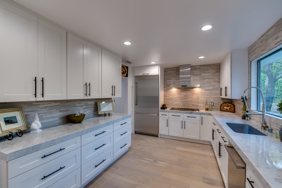 Inspiration for a mid-sized transitional u-shaped light wood floor eat-in kitchen remodel in Los Angeles with an undermount sink, shaker cabinets, white cabinets, marble countertops, beige backsplash, marble backsplash and stainless steel appliances