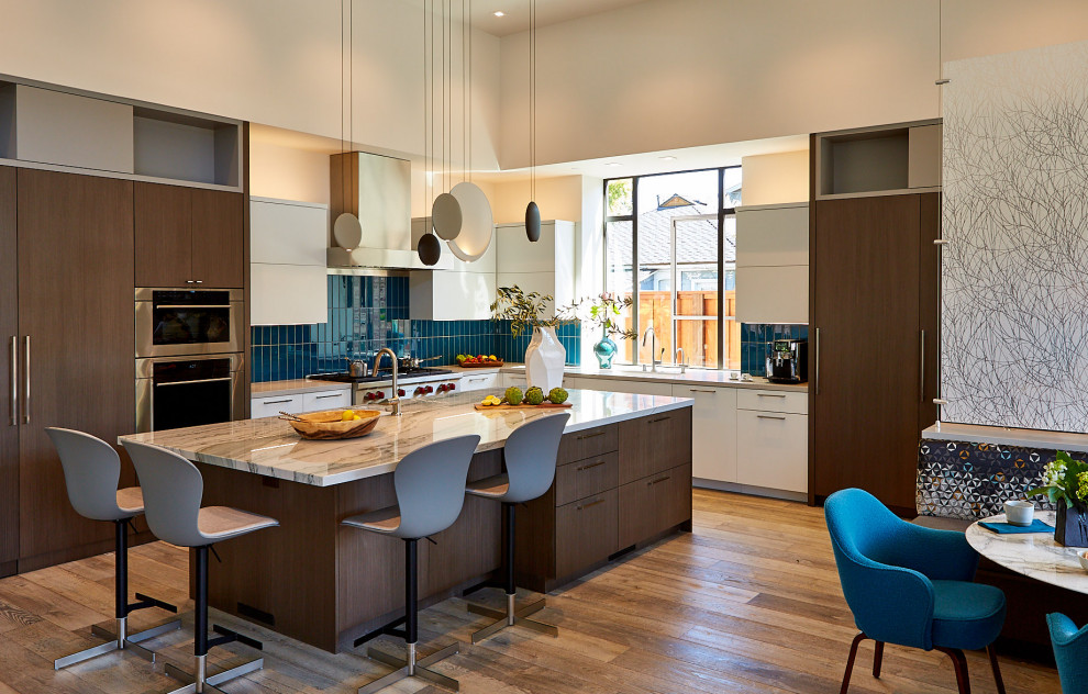 Photo of a large contemporary l-shaped kitchen/diner in San Francisco with flat-panel cabinets, engineered stone countertops, blue splashback, glass tiled splashback, an island, grey worktops, a submerged sink, white cabinets, integrated appliances, medium hardwood flooring and brown floors.