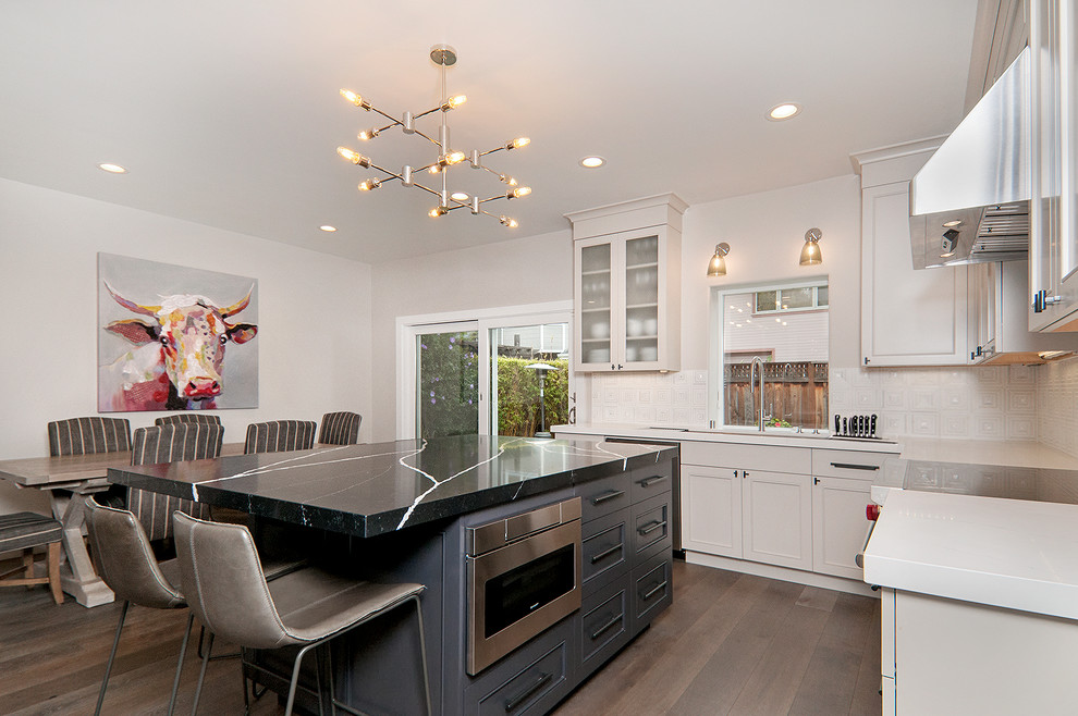 Example of a mid-sized transitional u-shaped medium tone wood floor and gray floor eat-in kitchen design in San Francisco with an undermount sink, recessed-panel cabinets, white cabinets, quartz countertops, white backsplash, stone tile backsplash, stainless steel appliances, an island and white countertops