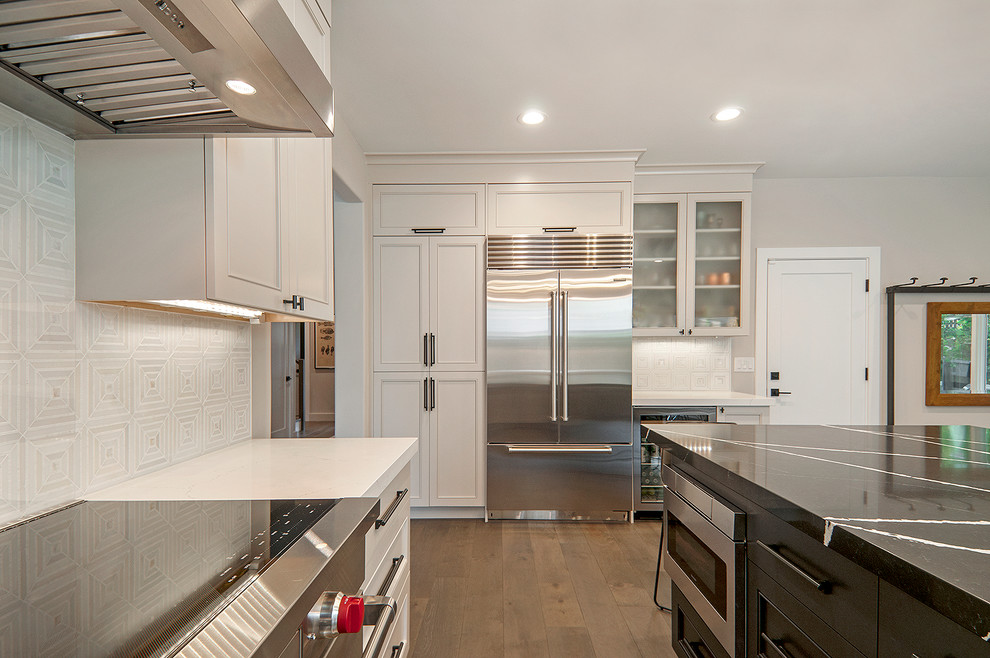 Exempel på ett mellanstort klassiskt vit vitt kök, med en undermonterad diskho, luckor med infälld panel, vita skåp, bänkskiva i kvarts, vitt stänkskydd, stänkskydd i stenkakel, rostfria vitvaror, mellanmörkt trägolv, en köksö och grått golv