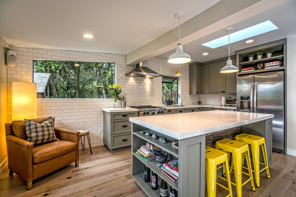 Photo of a medium sized classic u-shaped kitchen/diner in San Francisco with shaker cabinets, grey cabinets, white splashback, metro tiled splashback, stainless steel appliances, an island, a submerged sink, light hardwood flooring, engineered stone countertops, beige floors and white worktops.