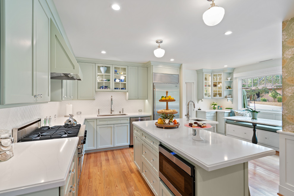 Inspiration for a mid-sized timeless medium tone wood floor and brown floor eat-in kitchen remodel in San Francisco with an undermount sink, shaker cabinets, green cabinets, quartz countertops, white backsplash, ceramic backsplash, stainless steel appliances, an island and white countertops